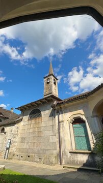 Cinematic video of a stone chapel framed by an arched passage on a bright summer day in Italy. Historic architecture, sunlit textures, and peaceful atmosphere in the countryside