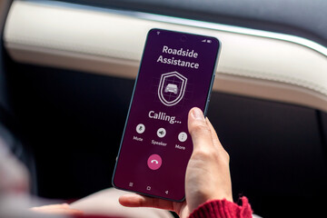 A woman in a car calling the roadside assistance service on her smartphone for help