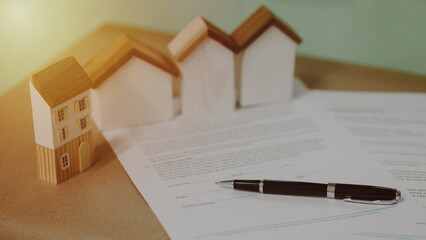 Real estate contract with pen and miniature houses on wooden desk, representing property agreement,...