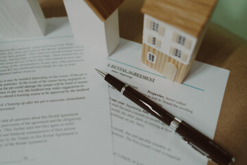 Real estate contract with pen and miniature houses on wooden desk, representing property agreement,...