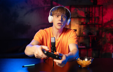 Excited young gamer streaming live with headphones, microphone, and controller in neon-lit room...