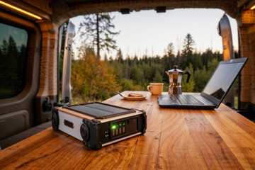 Van life digital nomad. A remote work setup with a laptop and portable power station inside a camper van with a forest view.