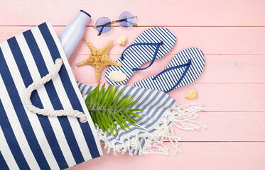 Blue beach bag with summer accessories on wooden background, top view