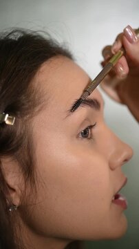 Close-up of eyebrows on which permanent eyebrow makeup is performed, combing eyebrow hairs with a brush. Permanent makeup procedure, performing PMU of eyebrows