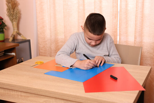 A boy makes applications from colored paper while sitting at a table. The concept of creativity and leisure.
