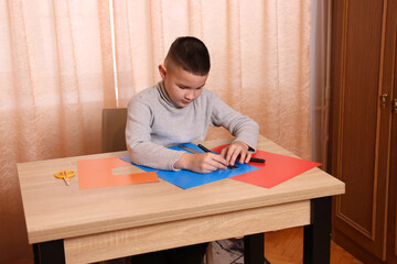 A boy makes applications from colored paper while sitting at a table. The concept of creativity and leisure.