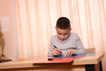 A boy makes applications from colored paper while sitting at a table. The concept of creativity and leisure.