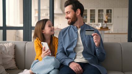 Joyful Caucasian parent man father holding credit card guy male talking finance smiling little...