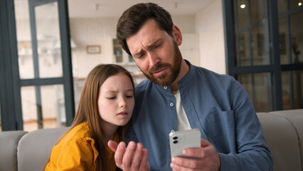 Stressed upset Caucasian family look mobile phone screen unhappy little daughter speaking dad man...