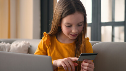 Parental control. Cheerful smiling Caucasian little girl child using banking card credit laptop...