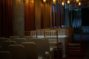 An elegant, dimly lit event venue with empty covered chairs and a formal table, creating an...