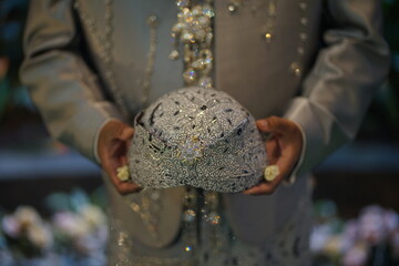 Groom in ornate traditional attire holding a symbolic rice offering during a sacred cultural...