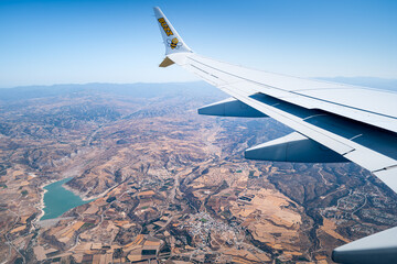 Wing of a Ryanair plane flying over an island with turquoise sea, Cyprus.
