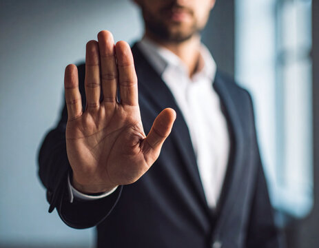 A close-up of a businessman in a suit holding his palm up in a distinct 'stop' gesture, conveying a firm message of refusal or limit setting. Ideal for concepts of business ethics, boundaries, and dec