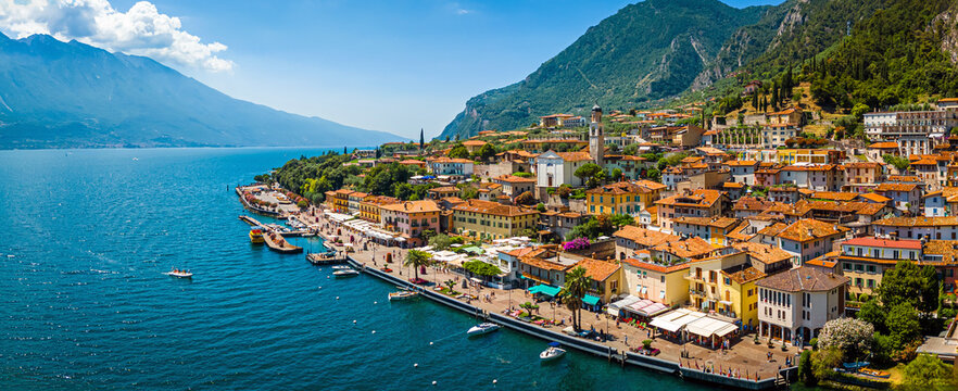 Aerial view of Limone sul Garda, a colorful lakeside town in Italy nestled between Lake Garda and steep mountains under a bright blue sky