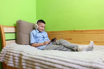 A boy in headphones listens to music from a smartphone while lying on the couch.