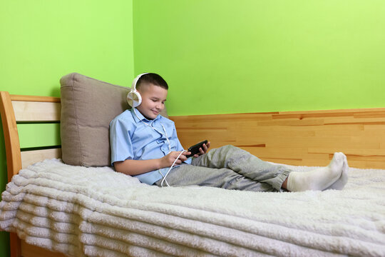A boy in headphones listens to music from a smartphone while lying on the couch.