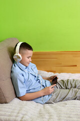 A boy in headphones listens to music from a smartphone while lying on the couch.