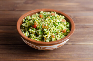 Oriental salad Tabbouleh in a ceramic bowl on a wooden table. Concept of traditional Lebanese or Syrian cuisine. Vegetarian or vegan dish. Rustic style. Selective focus. Horizontal orientation.