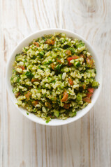 Oriental salad Tabbouleh in a white bowl on a wooden table. Concept of traditional Lebanese or Syrian cuisine. Vegetarian or vegan dish. Selective focus. Vertical orientation. Top view.