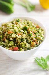 Oriental salad Tabbouleh in a white bowl on a wooden table. Concept of traditional Lebanese or...