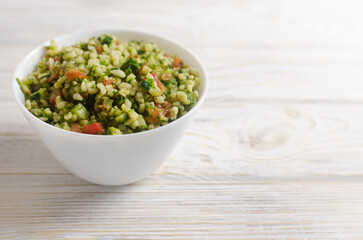 Oriental salad Tabbouleh in a white bowl on a wooden table. Concept of traditional Lebanese or Syrian cuisine. Vegetarian or vegan dish. Selective focus. Horizontal orientation. Copy space