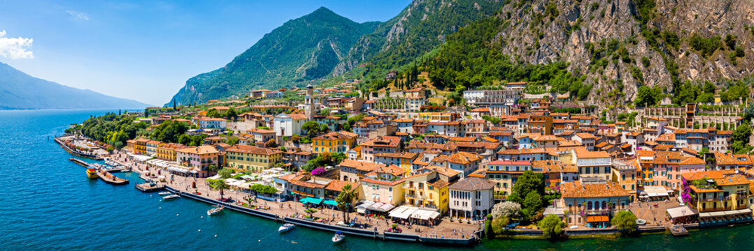 Aerial view of Limone sul Garda, a colorful lakeside town in Italy nestled between Lake Garda and steep mountains under a bright blue sky