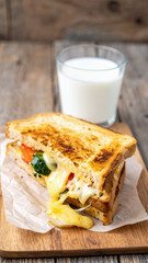 Cheese and vegetable toasted sandwich with glass of milk, comfort lunch, melted cheese pull, copy space, rustic table