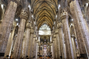 Gothic-style Milan Cathedral facade with ornate spires and intricate stonework against clear blue...