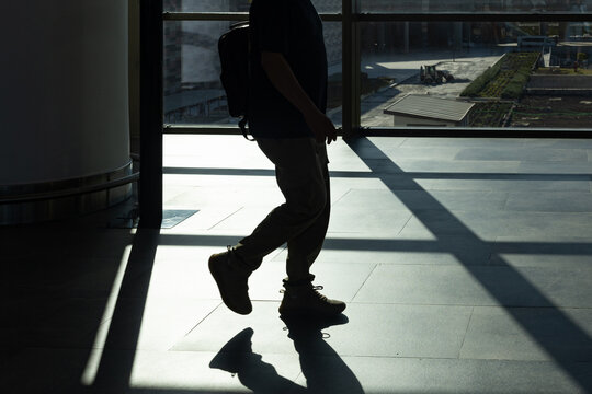 A silhouette of a walking traveler and their shadow reflected on a sunlit airport floor, capturing the mood of movement and departure.