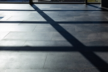 Sunlight casts geometric shadows of window frames on a polished airport floor, creating a...