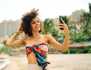 Portrait of young asian girl taking selfie while standing on the ocean beach after swimming. Beautiful pretty  female with sunglasses is photographing herself on the seaside using smartphone