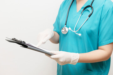 Healthcare worker in scrubs and gloves examining documents on clipboard, indicating focus on...