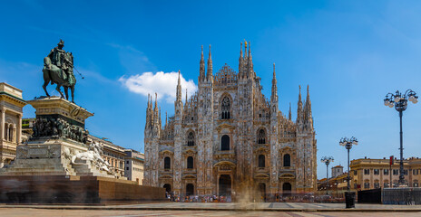Gothic-style Milan Cathedral facade with ornate spires and intricate stonework against clear blue...