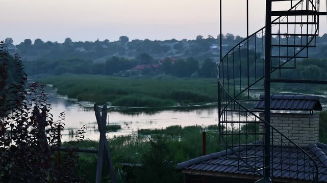 Time lapse showcasing persons ascending winding staircase against backdrop of lush greenery and tranquil waterway at dusk. Serene moment of nature and adventure over river Southern Bug in Ukraine