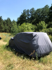 Vehicle covered with a tarp in a sunny forest clearing
