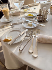 Elegant dining table setting with silver cutlery, pristine white plates, a glass of water, and coffee, conveying a sophisticated and serene breakfast or brunch ambiance