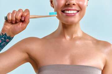 Close-up cropped image – a young woman with a bright white smile holding a toothbrush and smiling against a soft blue background.