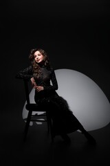 A girl in a long black dress stands near a black chair