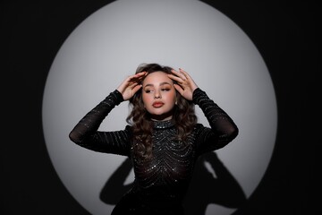 A girl in a long black dress stands near a black chair