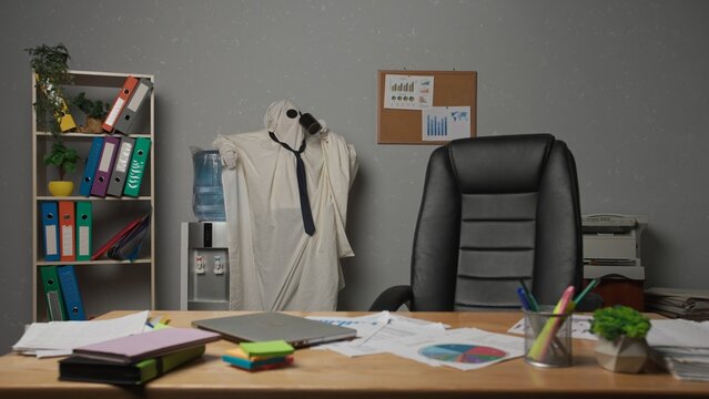 Halloween businessman ghost in white sheet standing in office drinking water, taking break during busy day. Happy halloween business concept.