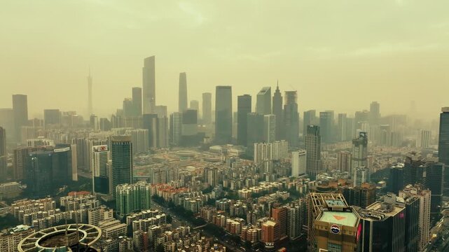 Guangzhou, China. Aerial view of a cityscape with a haze effect, showcasing a blend of modern skyscrapers and older buildings. The cityscape is dominated by a mix of highrise and lowrise structures.