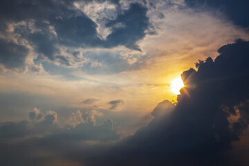 Dramatic cloudy sky with golden sunlight breaking through at sunset. A mix of dark storm clouds and...