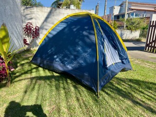 Tenda de campismo montada num relvado tropical sob uma palmeira num dia ensolarado. Ambiente tranquilo e perfeito para lazer ao ar livre.
