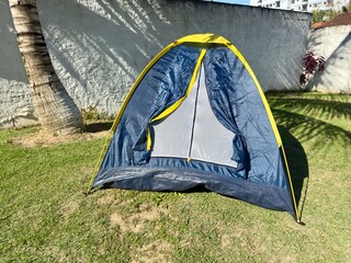 Tenda de campismo montada num relvado tropical sob uma palmeira num dia ensolarado. Ambiente tranquilo e perfeito para lazer ao ar livre.