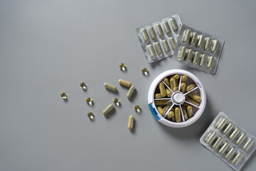 Daily vitamin routine featuring leafy green capsules and organized pill dispenser spread across a clean grey surface