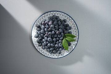 Fresh blueberries on a decorative plate with mint leaves, captured beautifully in natural light