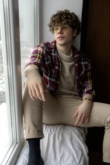 Young man relaxes by the window in cozy fashion during a winter afternoon in a softly lit room