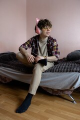 Young person enjoys music while relaxing in a cozy bedroom adorned with soft colors during a leisurely afternoon