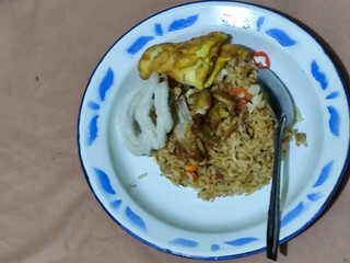 Fried rice with omelet, chicken pieces and red chili slices, has a delicious taste, served on a classic iron plate, with a brown background.